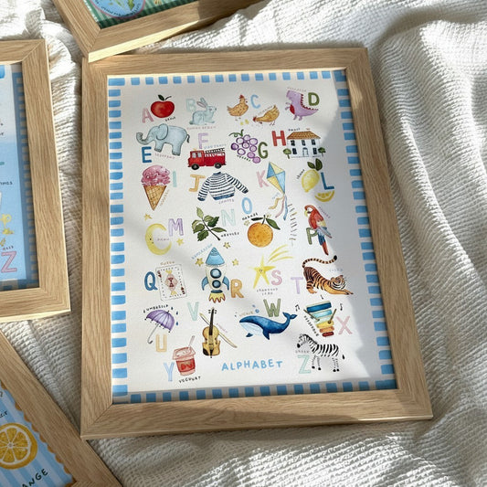 School Bus Studio alphabet nursery wall art print with hand-painted illustrations in a light wood frame.