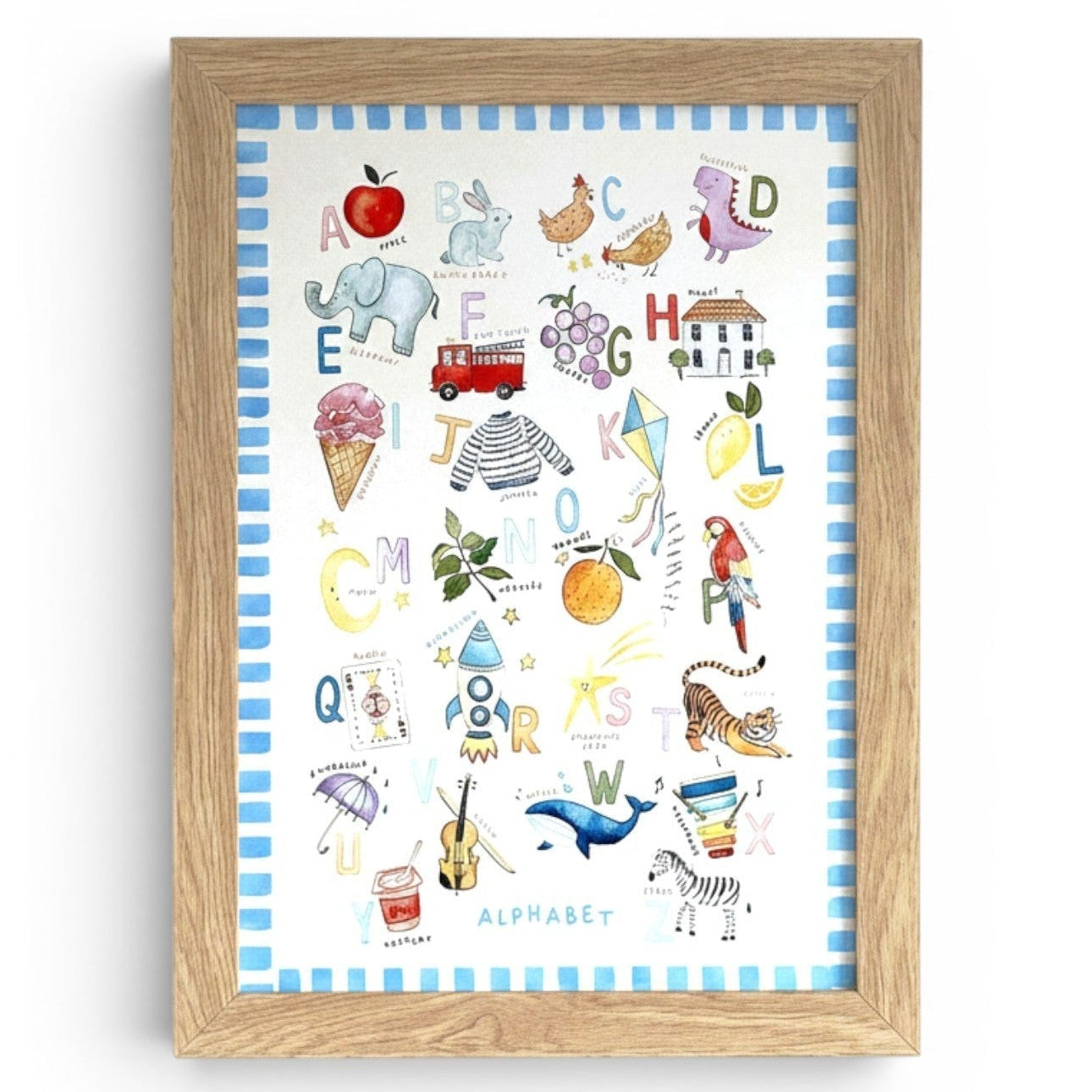 School Bus Studio illustrated alphabet nursery wall art print with hand-painted A-Z icons in a light wood frame.
